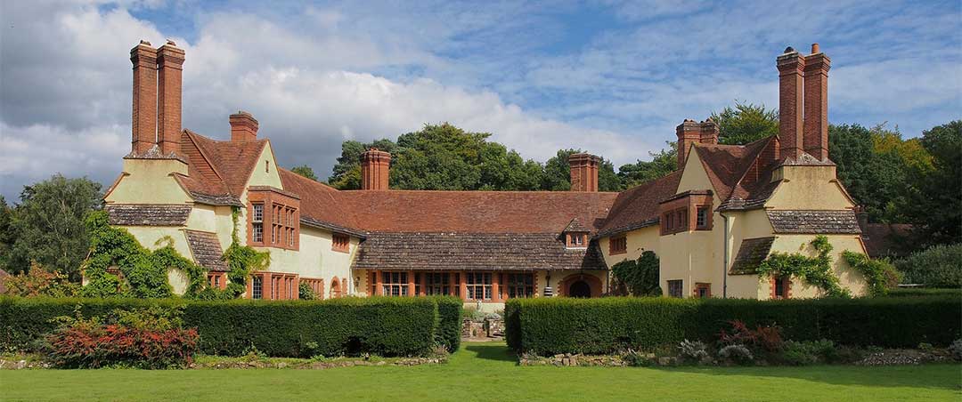 Large country cottage home with eight chimneys with a lush green landscaped yard and background