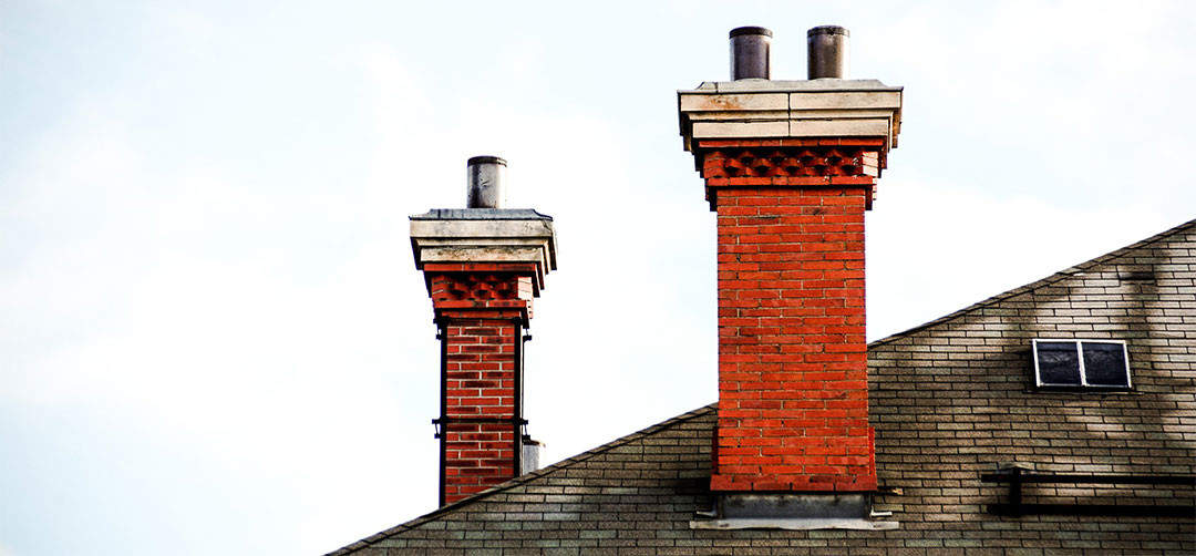 two chimneys with damaged masonry, rusted chase covers, and weathered chimney caps