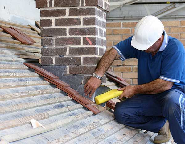 technician repairing chimney flashing while sitting on roof